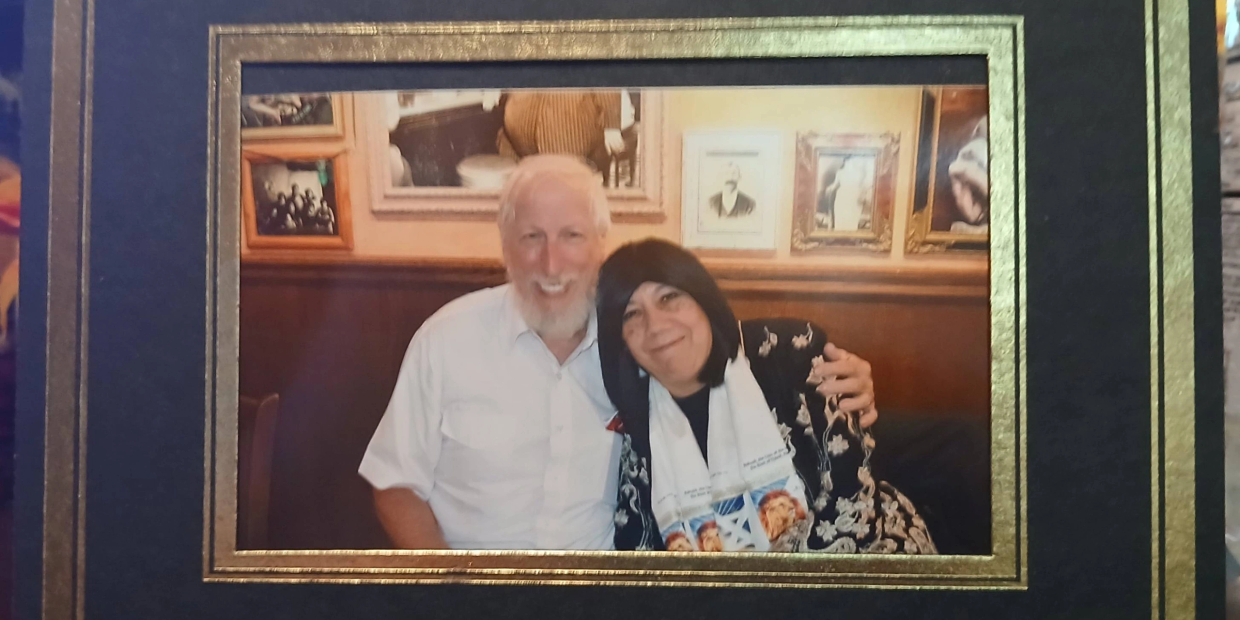 Smiling elderly couple posing together in a warmly decorated room with framed pictures.