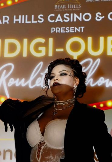Confident woman poses with dramatic makeup and jewelry against a casino event backdrop.