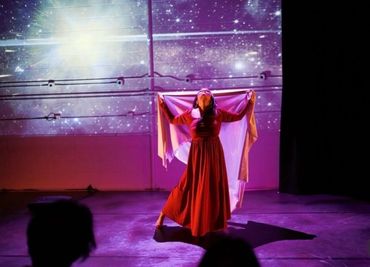 A dancer in a red dress performs under a starry sky projection.