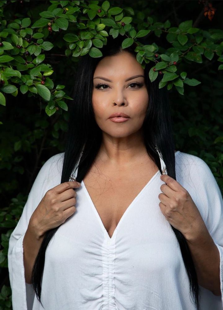 Woman in white dress framed by green leaves, holding her long black hair.