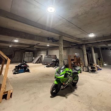 A green motorcycle parked in a spacious, unfinished basement with scattered equipment.