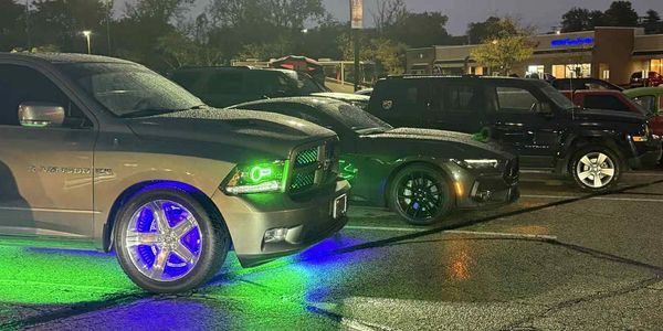 Cars lined up with colorful neon lights under streetlights at night.