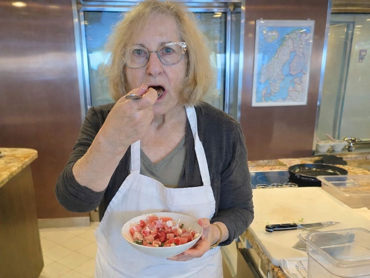Woman in apron tasting a fresh tomato salad in a kitchen.