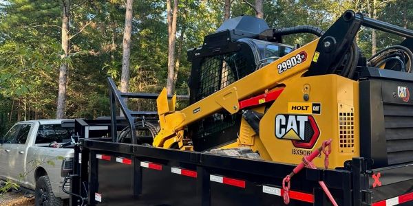 A Caterpillar skid steer with mulcher loaded on a trailer attached to a truck.