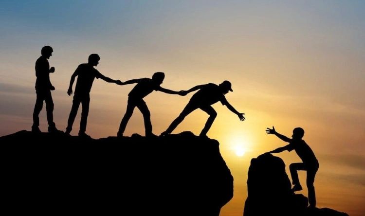 A group of people helping another person climb a mountain