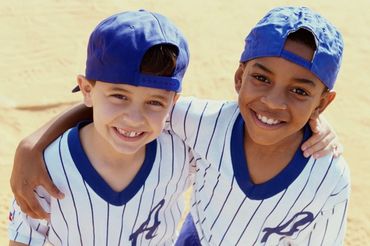 Two boys in baseball uniforms smiling with arms around each other.