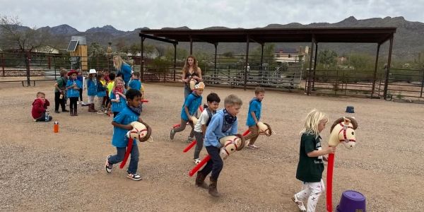 Children play horse race with stick horses outdoors.