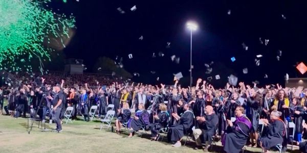Graduation ceremony with caps thrown and green confetti.