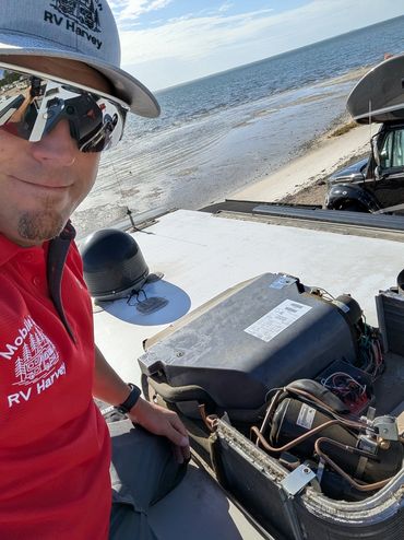 Man in RV Harvey shirt working on rooftop unit near a beach.