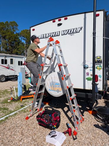 Man on ladder working on an Alpha Wolf camper trailer with tools nearby.