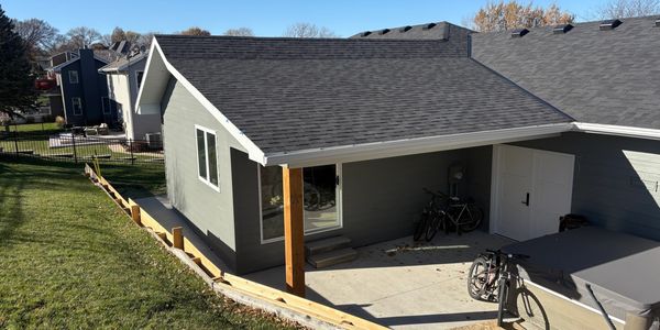 A gray backyard shed with bicycles and a hot tub under a clear blue sky.