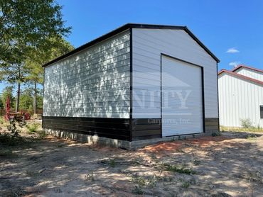 A black and white metal storage building with a roll-up door under a clear blue sky.