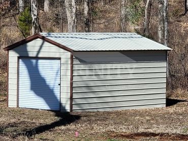 A small metal storage shed with a white rolling door in a wooded area.