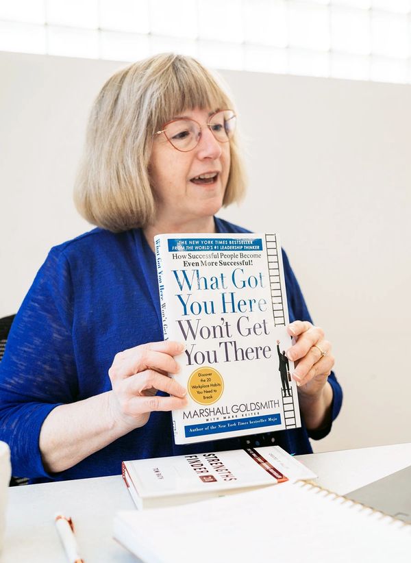 Financial consultant Susan Goodison holding a book and sitting at desk in blue jacket.