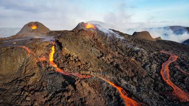 Two volcano crater erupting with lava in the background, with two lava flows on the foreground.