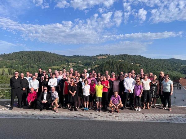Large group photo outdoors with hills and blue sky in background.
