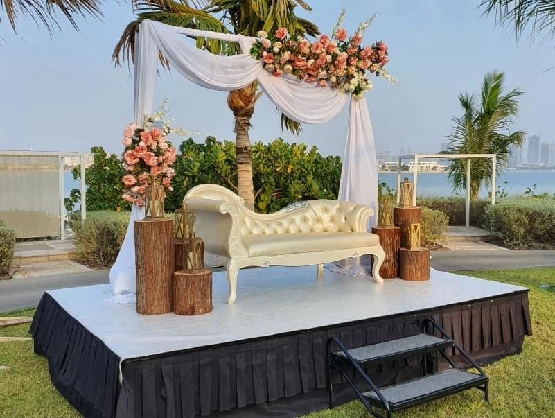 Elegant outdoor wedding stage with white sofa and floral decorations.