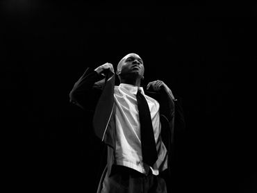 Black and white image of a man adjusting his jacket and looking upward.