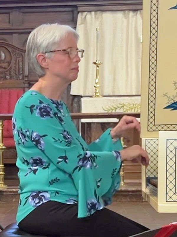 A woman in a floral turquoise blouse plays a keyboard instrument in a church setting.