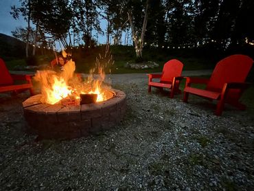 Cozy outdoor fire pit surrounded by red chairs at dusk.