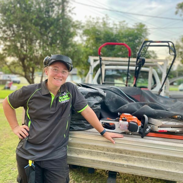 Shay the owner and operator of Blades & Blooms Lawn Care standing by her work vehicle with equipment