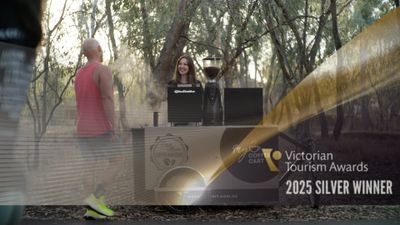 A man in a red tank top walking towards a smiling barista at a coffee cart in a wooded area.
