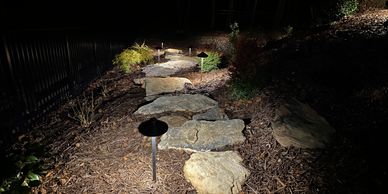 Stone pathway lit by ground lights at night.