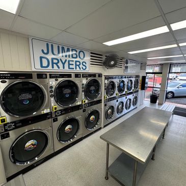 Interior of a laundromat with jumbo dryers and a folding table.
