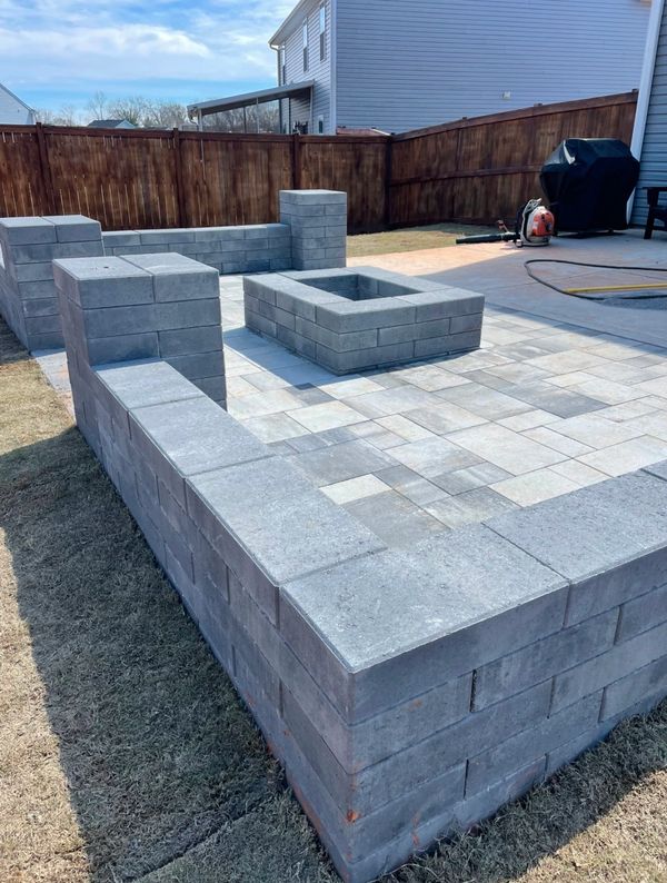 A backyard patio with a stone fire pit and seating walls under a clear sky.