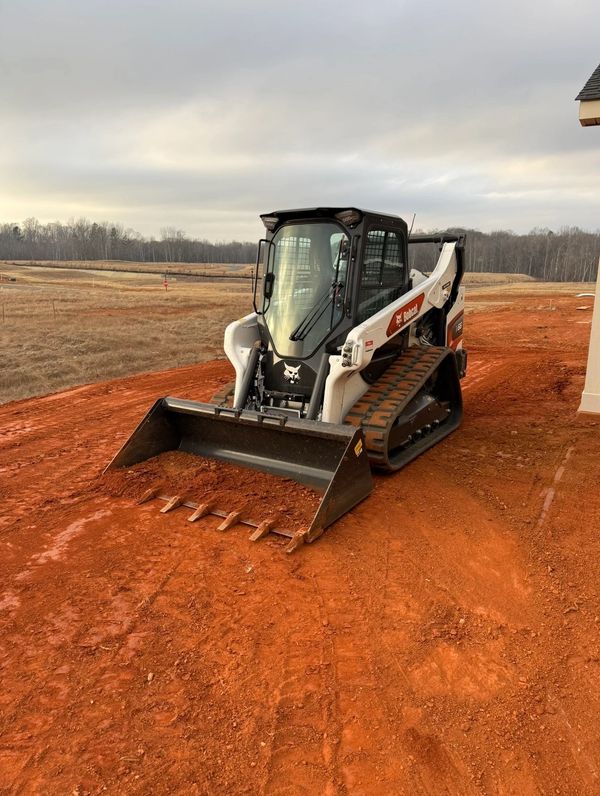 A Bobcat compact track loader on a red dirt construction site.