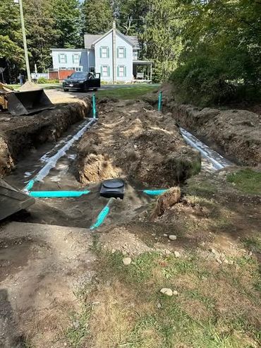 Construction site showing trench and plumbing pipes near a house.