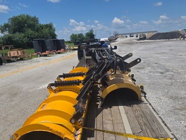 Yellow snowplow blades secured on a flatbed trailer under a clear sky.