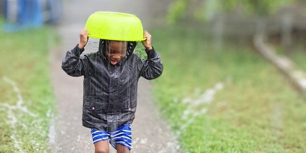 Child playing in the rain with a green basin on their head.