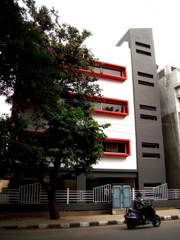 Modern building with red window frames and a motorbike passing by.