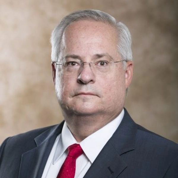 Man in a suit with red tie and glasses posing for a formal portrait.