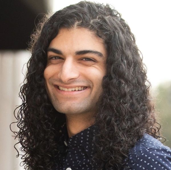 Smiling man with long curly hair wearing a patterned dark shirt.