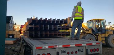 Worker standing on flatbed truck loaded with steel beams.