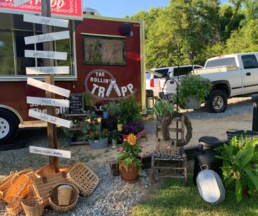Rustic outdoor setup with plants, baskets, and a food truck named 'The Rollin' Trapp'.