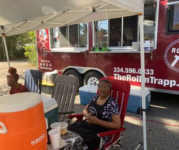 Two women sitting outside a red food truck under a white canopy.