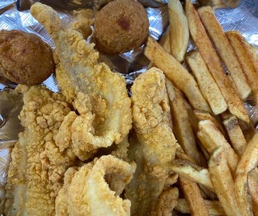 Fried catfish fillets, hush puppies, and seasoned French fries on foil.
