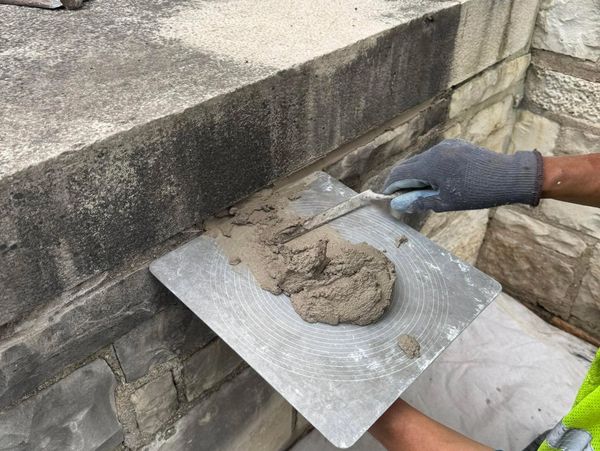 Worker applying mortar to stone wall with a trowel.