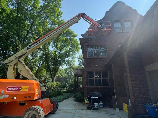 A boom lift is used for maintenance on a brick building under clear skies.