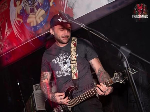 Man playing electric guitar on stage wearing an Oakland Raiders shirt.