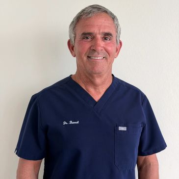 Male doctor in navy blue scrubs smiling.