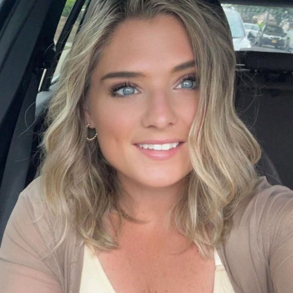 A woman with blonde hair smiles inside a car.