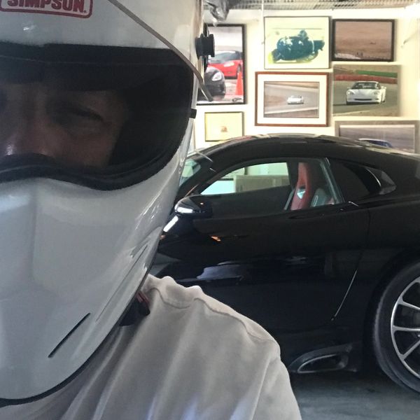 A man in a white helmet standing in front of a black Dodge Viper with racing pictures on the wall.