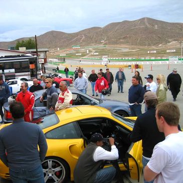 A group of people standing around a yellow Porsche in the pits of a race track