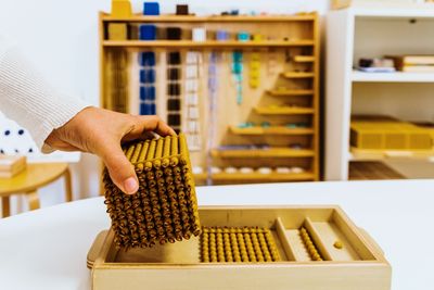 A Hand holing the thousand Golden bead cube in front of the Montessori Bead cabinet. 