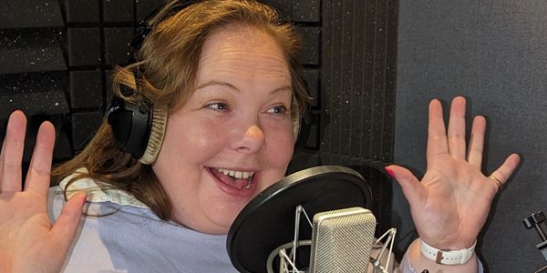 Woman smiling and talking into a microphone with headphones on.