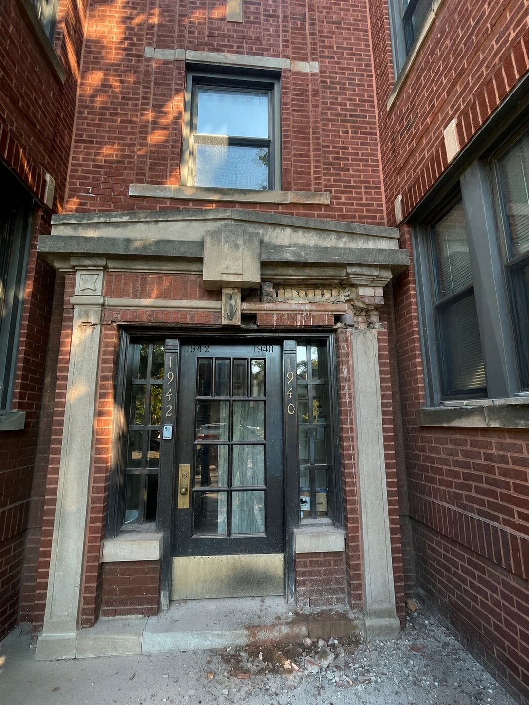Damaged entry with broken brick, cracked stone trim and visible deterioration above the doorway.